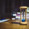close up of hourglass on the table with clock and books